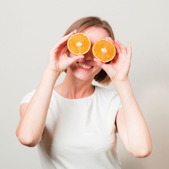 Smiling woman with orange slices in front of her eyes, symbolizing the importance of nutrition for eye health and promoting healthy vision