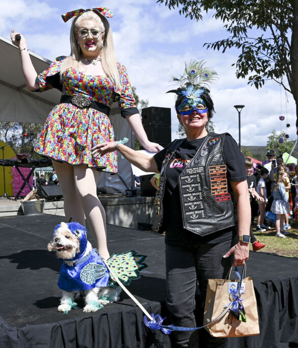 Two cheerful LGBTQIA+ individuals proudly posing with their fabulously dressed-up dog, symbolizing unity and celebration at the Coastal Twist Festival's Puparazzi Pooch Parade